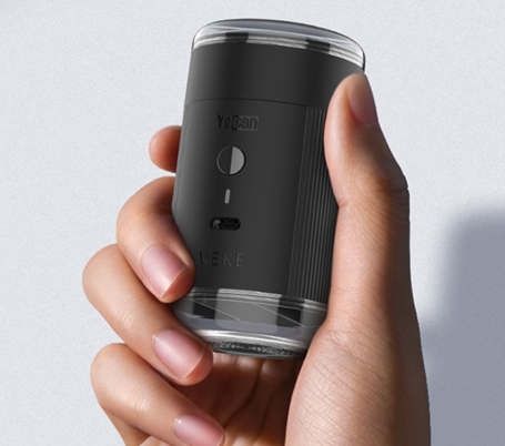 A hand holding a Yocan Yeke Electric Grinder with a clear top and bottom, featuring the brand name 'Yocan' and the model name 'VEKE'.